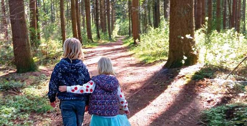 Zwei Kinder gehen Arm in Arm im Wald spazieren